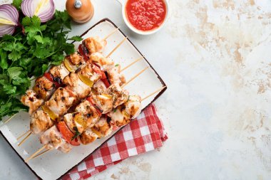 Tavuklu şiş kebap ya da seramik tabakta şiş kebap, baharatlar, kişniş otlar ve sebzeler beyaz masa arkasında. Gulaş ya da şiş kebap için mangal malzemesi. Üst Manzara. Boş kopyalama alanı.