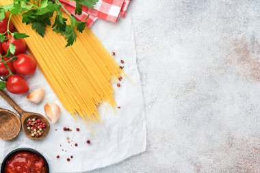 Makarna arka planı. Makarna spagetti, domates ketçap sosu, zeytinyağı, baharatlar, maydanoz ve açık gri bir masa üzerinde taze domatesler. Yemek pişirme geçmişi. Kopyalama alanı olan üst görünüm.