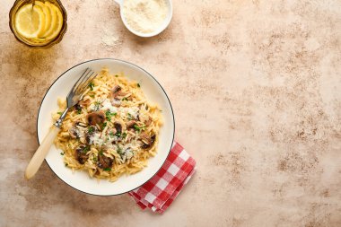 Italian pasta risoni, mushrooms, sauce, parmesan, thyme, garlic, olive oil, in white plate over slate, stone or concrete background. Top view with copy space. Italian cuisine.
