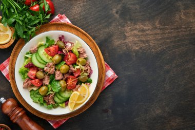 Taze sebzeli, zeytinli, kapari ve limonlu ton balığı salatası eski ahşap arka planda servis edilir. Kopyalama alanı olan üst görünüm.