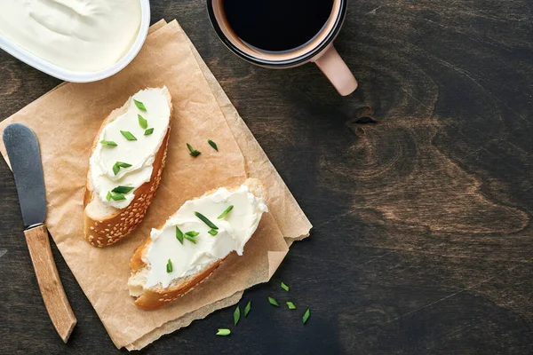 Yumuşak peynirli sandviç, yeşil soğanlı ve koyu ahşap arka planda ekmek. Ricotta sandviçi ve kahveyle basit bir kahvaltı. Metin için en üst görünüm kopyalama alanı.