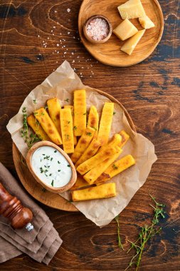 Ev yapımı polenta kızartması deniz tuzu, parmesan, kekik, yoğurt soslu biberiye. Tipik İtalyan kızarmış polentası. Kızarmış mısır çubukları. Ahşap arka plan. Üst görünüm