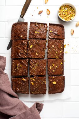 Fıstıklı çikolatalı kareler ve beyaz arkaplanda beyaz kağıt üzerinde çilek, üst manzara, yatay kompozisyon. Düz yiyecek.