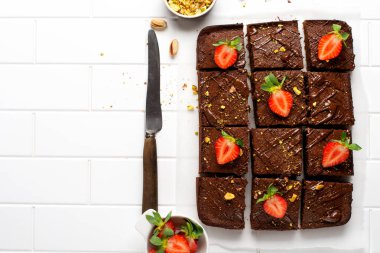 Fıstıklı çikolatalı kareler ve beyaz arkaplanda beyaz kağıt üzerinde çilek, üst manzara, yatay kompozisyon. Düz yiyecek.