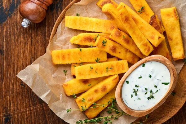 Ev yapımı polenta kızartması deniz tuzu, parmesan, kekik, yoğurt soslu biberiye. Tipik İtalyan kızarmış polentası. Kızarmış mısır çubukları. Ahşap arka plan. Üst görünüm