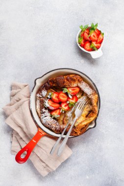Taze çilekli Hollanda bebek krepi ve beyaz mutfak arka planında kırmızı tavada krema şekeri serpiştirilmiş. Üst görünüm