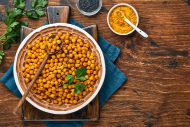 Eski ahşap masa arkasında seramik tabakta zerdeçal bulunan kızarmış nohut. Kızarmış baharatlı nohut ya da Hint chana 'sı ya da kolesistektomi, popüler atıştırma tarifi. Üst görünüm.