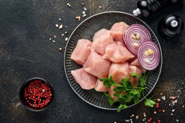 Tahtadaki tavuğun çiğ parçaları, baharatlar, otlar ve sebzeler koyu gri arka planda. Gulaş ya da şiş kebap için ham malzeme. Üst Manzara. Boş kopyalama alanı.