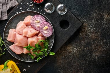 Tahtadaki tavuğun çiğ parçaları, baharatlar, otlar ve sebzeler koyu gri arka planda. Gulaş ya da şiş kebap için ham malzeme. Üst Manzara. Boş kopyalama alanı.