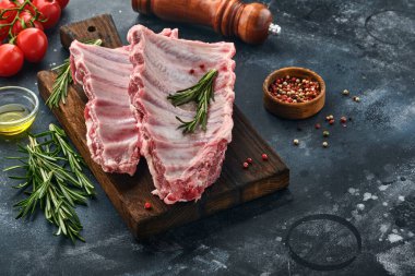 Çiğ domuz kaburgası ya da baharatlı, siyah ahşap tepside kırmızı biber, sarımsak karanfili ve otlu taze et. Metin için kopyalama alanı olan koyu dokulu arkaplan.