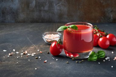 Eski ahşap arka planda bir bardak taze domates suyu, tuz, fesleğen ve domates standı. Kopyalama alanı ile.