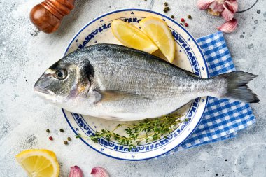 Çiğ dorado taze balığı ya da limon, kekik, sarımsak, kiraz, domates ve açık gri kayrak, taş ya da beton arkaplanda tuz yapımında kullanılan malzemelerle birlikte deniz çerezi. Kopyalama alanı olan üst görünüm.