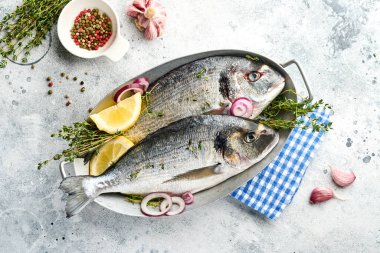 Çiğ dorado taze balığı ya da limon, kekik, sarımsak, kiraz, domates ve açık gri kayrak, taş ya da beton arkaplanda tuz yapımında kullanılan malzemelerle birlikte deniz çerezi. Kopyalama alanı olan üst görünüm.