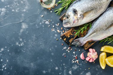 Çiğ dorado taze balığı ya da limon, kekik, sarımsak, kiraz, domates ve tuz yapımında kullanılan malzemelerle birlikte siyah kayalık, taş ya da beton zemin. Kopyalama alanı olan üst görünüm.