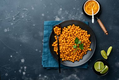 Kızarmış nohut, maydanozlu zerdeçal ve siyah tabakta limon, eski bir siyah masa arkasında. Kızarmış baharatlı nohut ya da Hint chana 'sı ya da kolesistektomi, popüler atıştırma tarifi. Üst görünüm.