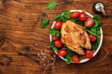 Ispanak yeşili salata, biber ve kiraz domatesli ızgara tavuk göğsü eski ahşap masa arka planında seramik bir tabakta. Üst görünüm.