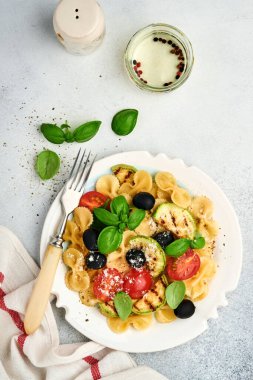 Sebzeli makarna fiocchi salatası ızgara kabak, vişneli domates, zeytin, fesleğen ve parmesan peyniri beyaz tabakta taş ya da beton arka planda. Yemek konsepti. Üst görünüm.