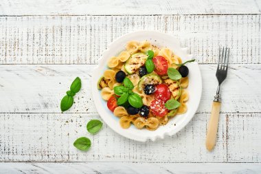 Sebzeli makarna fiocchi salatası ızgara kabak, vişneli domates, zeytin, fesleğen ve parmesan peyniri beyaz tabakta taş ya da beton arka planda. Yemek konsepti. Üst görünüm.