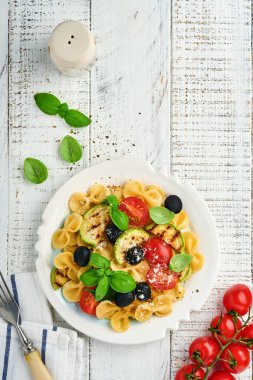 Sebzeli makarna fiocchi salatası ızgara kabak, vişneli domates, zeytin, fesleğen ve parmesan peyniri beyaz tabakta taş ya da beton arka planda. Yemek konsepti. Üst görünüm.