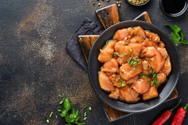 Teriyaki soya sosunda marine edilmiş çiğ tavuk eti, soğan ve biber siyah bir tabakta, taş, beton arka planda. Kopyalama alanı olan üst görünüm.