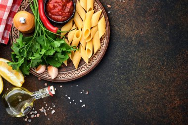 Makarna arka planı. Makarna rigati, domates ketçap sosu, zeytinyağı, baharatlar, maydanoz ve siyah bir masa üzerinde taze domatesler. Yemek pişirme geçmişi. Kopyalama alanı olan üst görünüm.