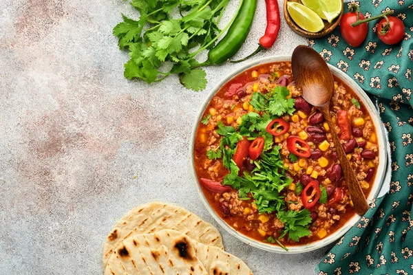 Mexican black bean soup with minced meat, tomato, cilantro, avocado and vegetables stew on a light grey slate, stone or concrete background. Traditional Mexican dish. Top view with copy space.