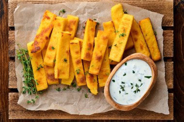 Ev yapımı polenta kızartması deniz tuzu, parmesan, kekik, yoğurt soslu biberiye. Tipik İtalyan kızarmış polentası. Kızarmış mısır çubukları. Ahşap arka plan. Üst görünüm.