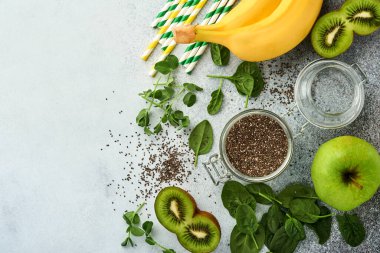 Yeşil smoothie, taze organik ıspanaklı bezelye mikroçim, muz, kivi, elma ve chia tohumu için açık gri beton zemin. Sağlıklı beslenme malzemeleri. Üst görünüm, alanı kopyala