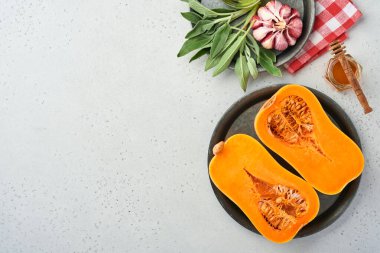 Yarım parça çiğ organik tereyağlı kabak, adaçayı yaprağı, çok renkli sarımsak, bal, tuz ve biber beyaz bir tahta, taş ya da beton arka planda. Yemek arkaplanı. Kopyalama alanı olan üst görünüm.