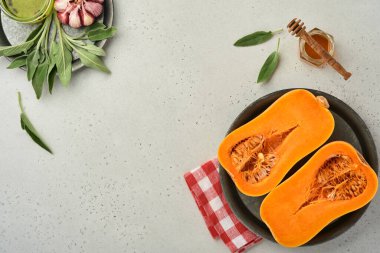 Yarım parça çiğ organik tereyağlı kabak, adaçayı yaprağı, çok renkli sarımsak, bal, tuz ve biber beyaz bir tahta, taş ya da beton arka planda. Yemek arkaplanı. Kopyalama alanı olan üst görünüm.