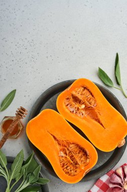 Yarım parça çiğ organik tereyağlı kabak, adaçayı yaprağı, çok renkli sarımsak, bal, tuz ve biber beyaz bir tahta, taş ya da beton arka planda. Yemek arkaplanı. Kopyalama alanı olan üst görünüm.