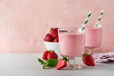 İki çilekli smoothie ya da böğürtlenli milkshake ve açık pembe arka planda nane şekeri. Yaz içeceği, milkshake ve ferahlatıcı organik konsept. Sağlıklı beslenme, vejetaryen gıda konsepti.