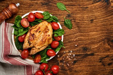 Ispanak yeşili salata, biber ve kiraz domatesli ızgara tavuk göğsü eski ahşap masa arka planında seramik bir tabakta. Üst görünüm.
