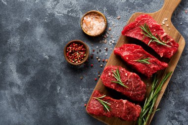 Baharatlı, soğanlı ve biberiyeli çiğ biftek. Koyu levha ya da beton arka plan. Üst görünüm