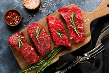 Baharatlı, soğanlı ve biberiyeli çiğ biftek. Koyu levha ya da beton arka plan. Üst görünüm