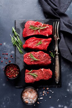 Baharatlı, soğanlı ve biberiyeli çiğ biftek. Koyu levha ya da beton arka plan. Üst görünüm
