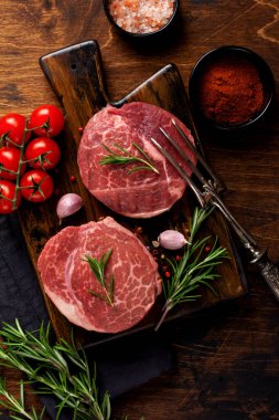 Ahşap tahtada iki taze Paris usulü çiğ biftek, eski ahşap arka planda tuz, biber ve rosmary. Kara Angus. Üst görünüm