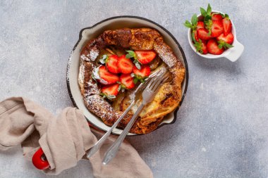 Taze çilekli Hollanda bebek krepi ve beyaz mutfak arka planında kırmızı tavada krema şekeri serpiştirilmiş. Üst görünüm