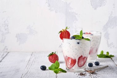 İki çilekli chia tohumu katmanlı smoothie veya açık gri arka planda çilekli ve yaban mersinli naneli milkshake. Yaz ve sağlıklı diyet içecekleri, vejetaryen gıda konsepti..