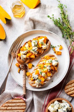 Fırında balkabağı ve mavi küflü Dorblu peynirli sandviç, bal ve kekik. Beton, eski, aydınlık arka planda. Üst görünüm