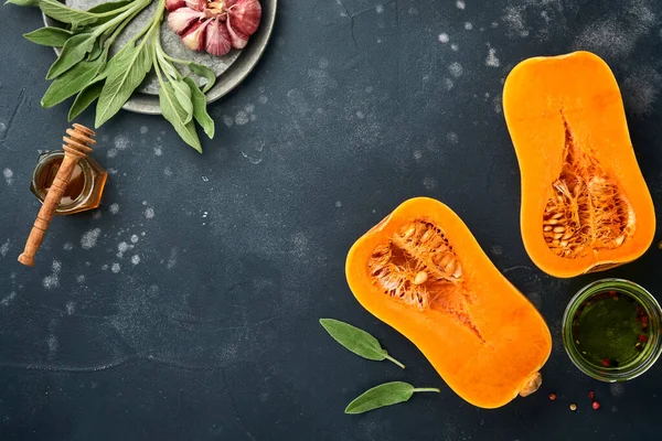 Yarım parça çiğ organik tereyağlı kabak, adaçayı yaprağı, çok renkli sarımsak, bal, siyah tahtada tuz ve biber, taş ya da beton arka plan. Yemek arkaplanı. Kopyalama alanı olan üst görünüm.