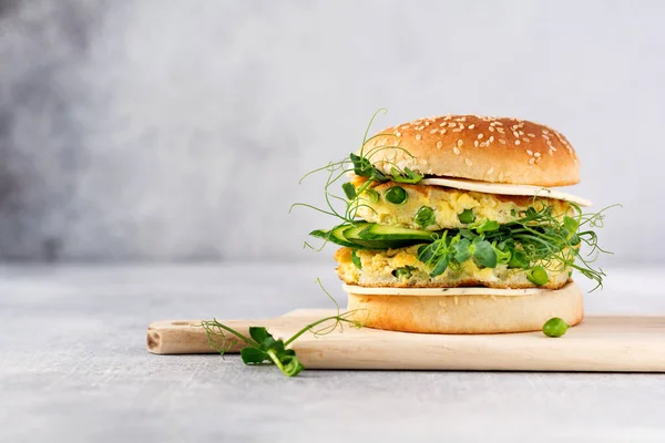 Burger healthy vegetarian with egg and pea shoots and seeds microgreen, fresh salad, cucumber slice on a cutting wooden board on light background. Selective focus