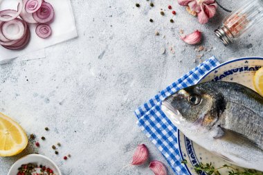 Çiğ dorado taze balığı ya da limon, kekik, sarımsak, kiraz, domates ve açık gri kayrak, taş ya da beton arkaplanda tuz yapımında kullanılan malzemelerle birlikte deniz çerezi. Kopyalama alanı olan üst görünüm.