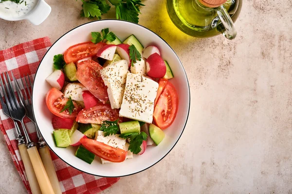 stock image Radish, cucumber, tomato, pepper and feta cheese with spices pepper and olive oil in white bowl on grey slate, stone or concrete background. Healthy food concept. Top view.