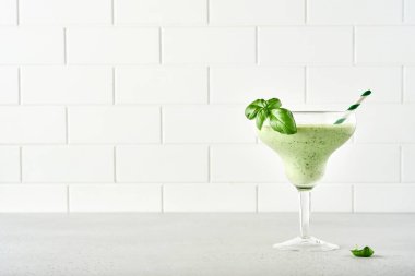 Taze fesleğen yaprağıyla süslenmiş yeşil sebze suyu ya da meyve püresi açık gri kayrak, taş ya da beton arka planda. Kopyalama alanı olan üst görünüm.