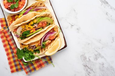 Beyaz taş masada ızgara tavuk, avokado, mısır taneleri, domates, soğan, kişniş ve salsa soslu Meksika tacoları. Geleneksel Meksika ve Latin Amerika sokak yemekleri. Üst görünüm.