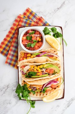 Beyaz taş masada ızgara tavuk, avokado, mısır taneleri, domates, soğan, kişniş ve salsa soslu Meksika tacoları. Geleneksel Meksika ve Latin Amerika sokak yemekleri. Üst görünüm.