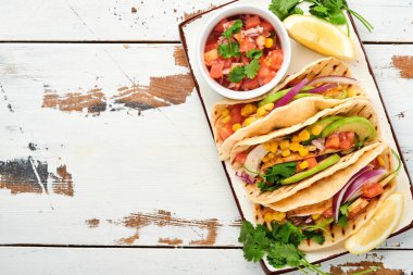 Beyaz taş masada ızgara tavuk, avokado, mısır taneleri, domates, soğan, kişniş ve salsa soslu Meksika tacoları. Geleneksel Meksika ve Latin Amerika sokak yemekleri. Üst görünüm.