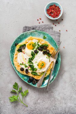 Türk yumurtaları yoğurt, peynir, zeytin, ıspanak ve gri arka planda seramik vintage tabakta kırmızı biber. Üst görünüm.