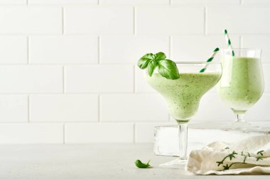 Taze fesleğen yaprağıyla süslenmiş yeşil sebze suyu ya da meyve püresi açık gri kayrak, taş ya da beton arka planda. Kopyalama alanı olan üst görünüm.
